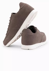 Grå mockaskor med låg profil, vit gummisula och subtila sömdetaljer. Snören är synliga på framsidan.