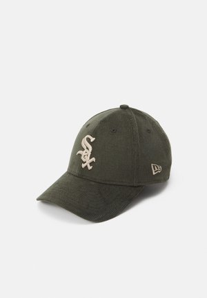 Olive green baseball cap made of ribbed fabric, featuring beige embroidered logo and accents. Curved brim and adjustable strap at the back.