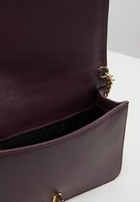 Borsa in pelle di un profondo viola con una texture liscia, dotata di una chiusura dorata e un'apertura superiore che rivela un rivestimento interno nero.