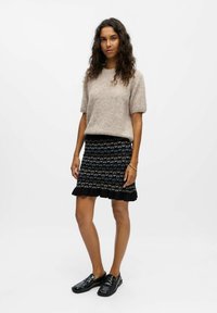 Pull tricoté en beige clair avec des manches courtes, assorti à une jupe noire à motifs avec un ourlet volanté et des accents bleus, ainsi qu'à des chaussures noires.