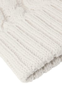 Bílý pletený béžový klobouk s ribbed texturou a vzorem kabelkového pletení. Měkká, hrubá příze s ohnutým okrajem pro zvýšené teplo.