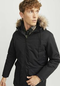 Sort parka-jakke med en hætte foret med faux pels, lynlås lukning, to forlommer og en glat tekstur. Subtilt design med funktionelle detaljer.