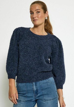 Navy blue fuzzy sweater with a round neckline, puffed sleeves, and a ribbed hem, paired with light blue high-waisted jeans.