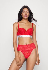 Punane pitsist rinnahoidja traadiga ja reguleeritavate rihmadega. Sobitatud kõrge vöökohaga pitsist püksikutega, millel on lillemustrid ja sile vöökoht.