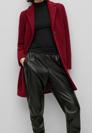 Bordeaux wollen jas met aangeknipte revers over een zwarte fitted top, gecombineerd met zwarte nepleer broek met een elastische tailleband.