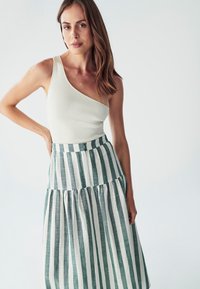 Jednoramenný biely rebrovaný top spárovaný so zeleno-bielo pruhovanou midi sukňou s rozšíreným tiered dizajnom.