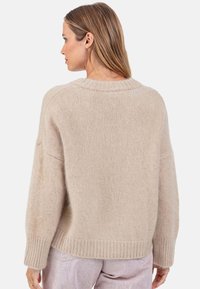 Beiger Strickpullover mit weitem, geripptem Ausschnitt und Bündchen. Der Stoff wirkt weich, mit lockerer Passform und überschnittenen Schulternähten.