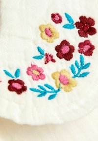 Bestickter Stoff mit kleinen Blumen in Pink, Gelb und Burgund, mit blauen Blättern auf weißem Textil.