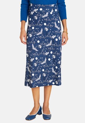 Midilange blaue Rock mit einem weißen Kranichmuster und kreisförmigen Akzenten, aus einem glatten Material hergestellt. Kombiniert mit blauen Absätzen.