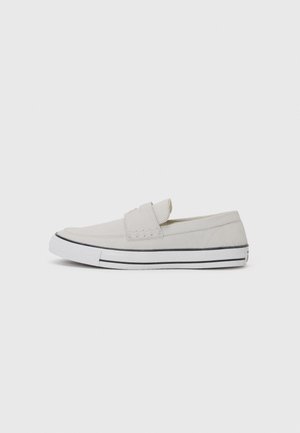 Zapatilla casual de color gris claro sin cordones con suela de goma blanca y raya negra, diseño de corte bajo y detalles cosidos a un lado.