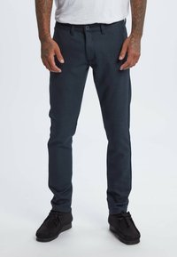 Dark blue trousers made of textured fabric featuring a slim fit, belt loops, and a single button closure. Worn with black shoes.