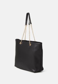 Bolsa tote sintética negra con un acabado suave, doble mango de cuero y cadena de oro, y detalles trenzados en un lado.
