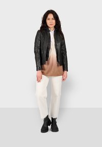 Čierna kožená bunda so zipsom a textúrovanými rukávmi, béžový ombre sveter, biele nohavice a čierne členkové čižmy s hrubou podrážkou.