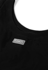 Zwart katoenen tanktop met een ronde halslijn en een textuur label met de tekst "10DAYS" op een rechthoekige zilveren patch aan de voorkant.