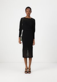 Melna ribota trikotāžas kleita ar garām piedurknēm un pieguļošu siluetu, ar caurspīdīgu paneļu akcentiem. Komplekts papildināts ar melniem siksniņu sandales un mazu somiņu.