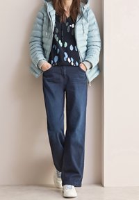 Puffig ljusblå jacka, marinblå topp med flerfärgade prickar, mörkblå vida jeans och vita sneakers. Avslappnad outfit med lager av texturer.