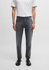 Grå denimjeans med en tapered fit, fem-lomme-design og subtile whiskers. Båret med en ensfarvet hvid skjorte og sorte dress sko.
