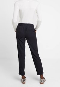 Zwarte broeken met een ontspannen pasvorm, een elastische tailleband en opgerolde manchetten, gecombineerd met een witte geribbelde top en gestreepte schoenen.