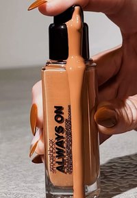 Bouteille de fond de teint Smashbox Always On, en verre avec un capuchon noir, contenant un liquide brun clair ; l'étiquette présente un texte noir. Fini brillant.