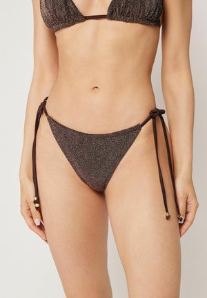 Kvinde iført mørkebrune glitrende bikiniunderdele med sidebånd og matchende bikinitop, vist fra hofter til bryst mod ensfarvet baggrund.