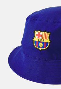 Blue bucket hat made of fabric, featuring a stitched shield logo with red, yellow, and blue details, including a soccer ball graphic.