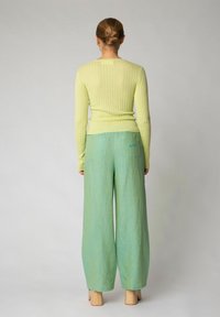 Maglietta lunga a maniche con ripresa verde chiaro abbinata a pantaloni larghi blu-verde chiaro con due tasche posteriori e un piccolo logo.