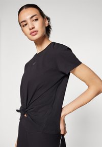 Zwarte t-shirt met korte mouwen en een geknoopt ontwerp in de taille, gemaakt van zachte stof, met subtiele stikdetails en een ronde hals.