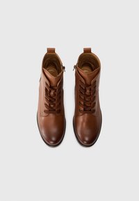 Botas de piel marrón hasta el tobillo con cordones, punta redonda y un zipper lateral. Textura suave y diseño minimalista. Forro interior visible.