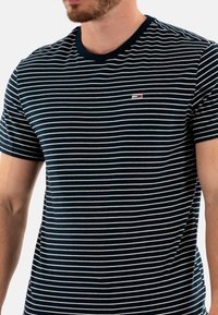 T-shirt rayé bleu marine avec des rayures blanches horizontales, col rond, manches courtes et un petit logo accentué sur la poitrine.