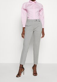 Chemise rose pâle à manches longues avec boutons, associée à un pantalon ajusté à motif pied-de-poule noir et blanc, et des talons hauts noirs à brides.