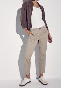 Beiga chinos med slim fit, kombinerat med en vit tanktopp och en brun oversized skjorta. Skorna är vita med grå och blå accenter.