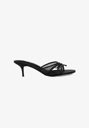 Sandalias negras de tacón con correas delgadas, un acento de lazo y una textura suave. Presentan una punta afilada y un tacón stiletto moderado.