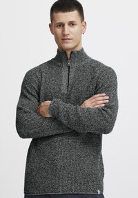 Schwarzer und grauer strukturierter Strickpullover mit einem halbseitigen Reißverschlusskragen und langen Ärmeln. Besitzt gerippte Bündchen und ein kleines Markenzeichen am Saum.