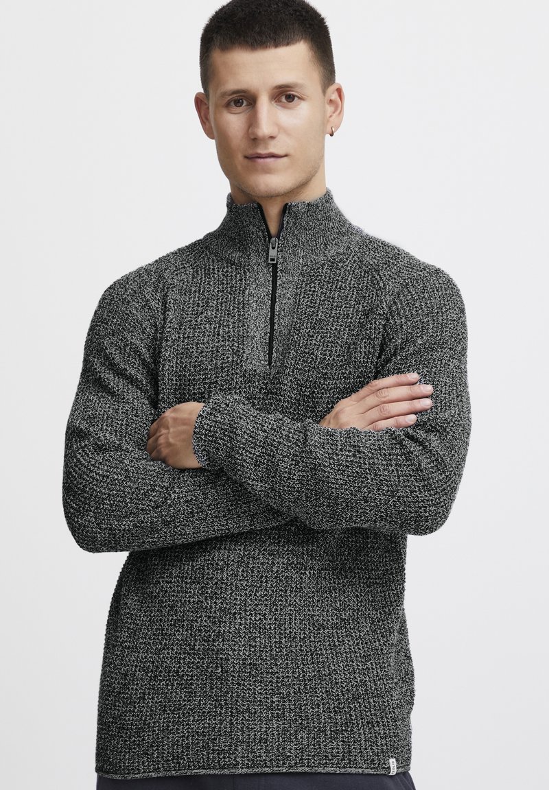 Schwarzer und grauer strukturierter Strickpullover mit einem halbseitigen Reißverschlusskragen und langen Ärmeln. Besitzt gerippte Bündchen und ein kleines Markenzeichen am Saum.