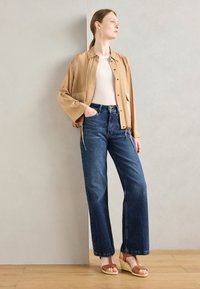 Light beige, long-sleeve shirt with pockets, paired with high-waisted blue jeans and brown strappy wedge sandals. Smooth fabric and relaxed fit.