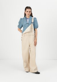 Camicia di jeans a maniche corte con grande colletto, abbinata a salopette beige a righe con gambe ampie e spalline regolabili.