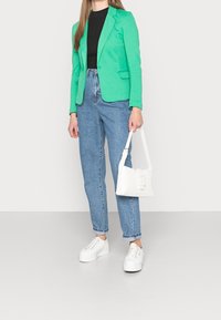 Blazer vert, haut côtelé noir, jean taille haute bleu clair, baskets à plateforme blanches et petit sac à main blanc.