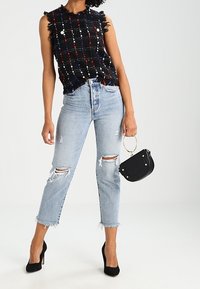 Haut sans manches à carreaux noirs et multicolores avec des bords effilochés, associé à un jean en denim bleu clair déchiré et des talons hauts noirs.