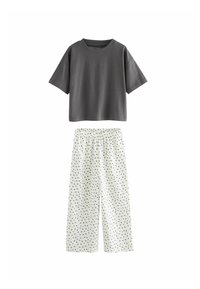 Graues T-Shirt mit kurzen Ärmeln, kombiniert mit weißen weit geschnittenen Hosen, die ein schwarzes Herzmuster und einen elastischen Bund haben.