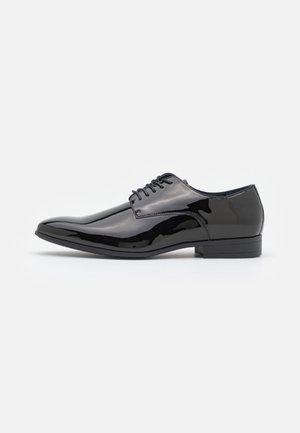 Chaussure habillée en cuir verni noir avec un design épuré, bout arrondi et lacets à l'avant. Dispose d'un petit talon et d'une finition lisse.