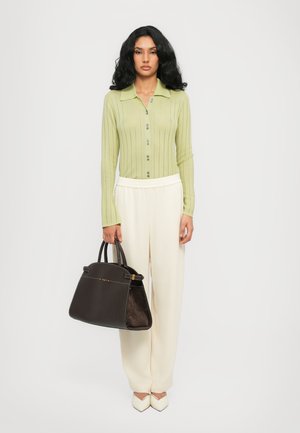 Maglietta lunga a maniche con righe verde chiaro e colletto, pantaloni ampi crema, décolleté bianchi a punta e una borsa a tracolla marrone scuro con contrasto di texture.