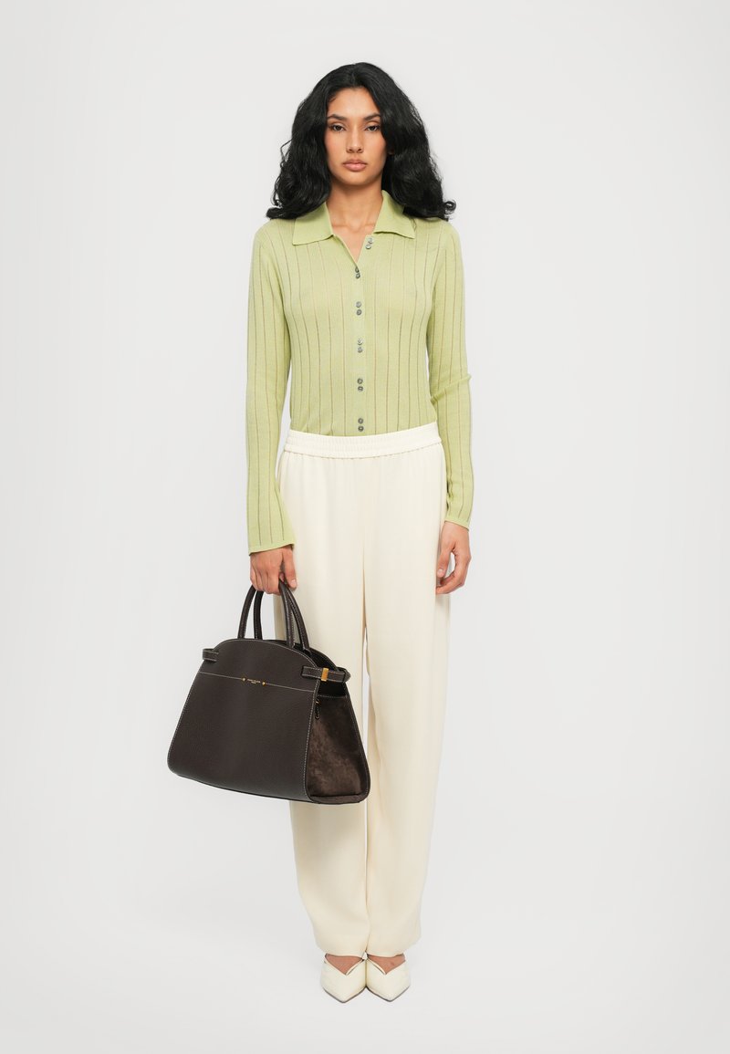Maglietta lunga a maniche con righe verde chiaro e colletto, pantaloni ampi crema, décolleté bianchi a punta e una borsa a tracolla marrone scuro con contrasto di texture.