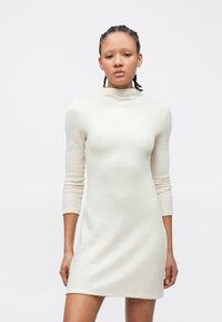 Rochie tricotată de culoare alb-crem, cu guler înalt, mâneci lungi, corp mulat și tiv evazat. Materialul are o textură striată.