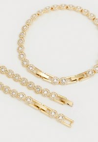 Gold-tone jewelry set featuring a necklace and matching bracelets, adorned with circular, pronged gemstones for added sparkle.
