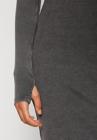 Robe à manches longues en tissu gris foncé, présentant des trous pour les pouces aux poignets et une silhouette ajustée, mettant en valeur les détails de texture et de forme.