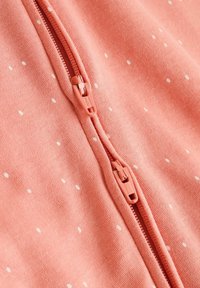 Pink fabric with white polka dots features a front zipper with matching zipper pulls, highlighting a soft, textured surface.