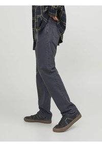 Pantalones de mezclilla gris oscuro con un diseño de pierna recta y un ligero desgaste. Llevados con zapatillas negras que presentan detalles texturizados.