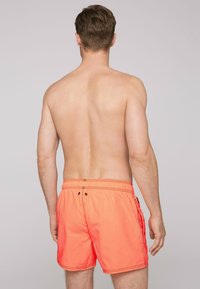 Narancssárga úszóshort elasztikus derékkal, kontrasztos fekete varrással és oldalsó zsebekkel, a hátulját mutatja egy mezítelen torzón.