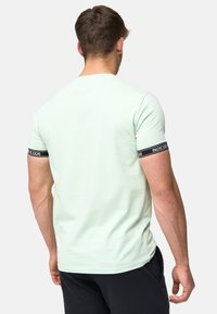 Camiseta de manga corta verde menta hecha de algodón, con una banda negra que lleva el texto "INDICODE" en la manga y un diseño ajustado.