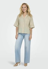Lyse beige kortærmet skjorte med knapper og brystlomme, parret med lyseblå vide jeans og nude højhælede sko.